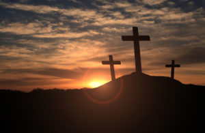 Three wooden crosses on a hill at sunset.